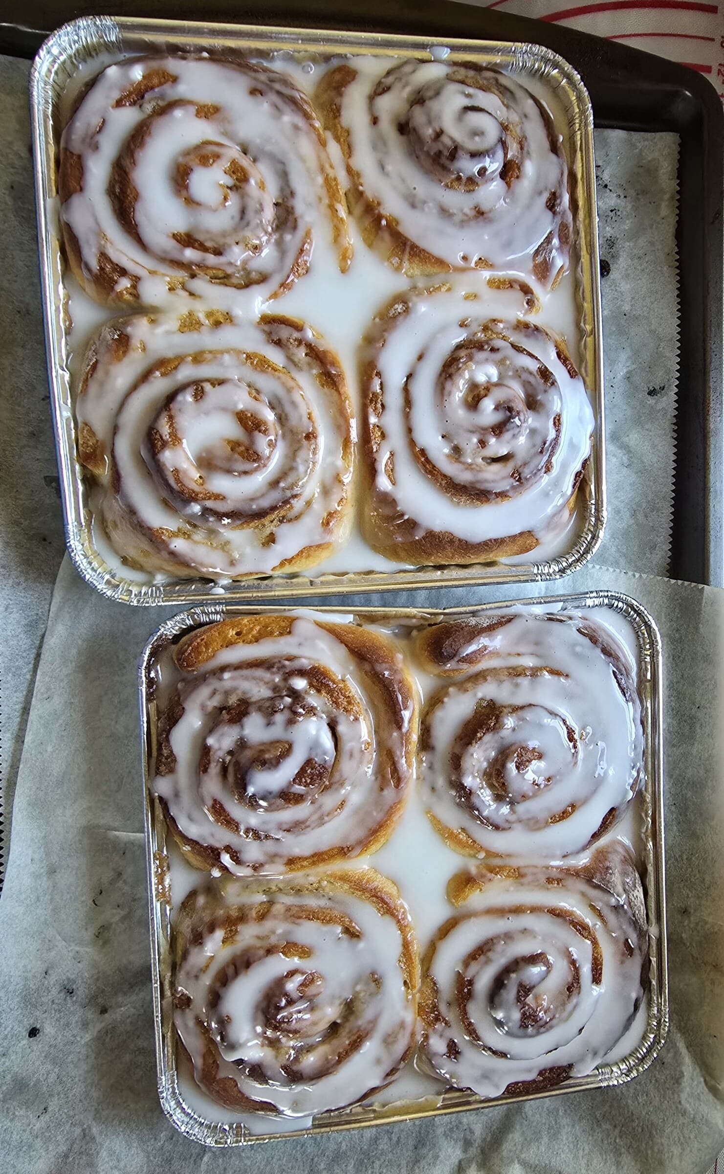 Two pans of cinnamon rolls covered with swirls of white icing.