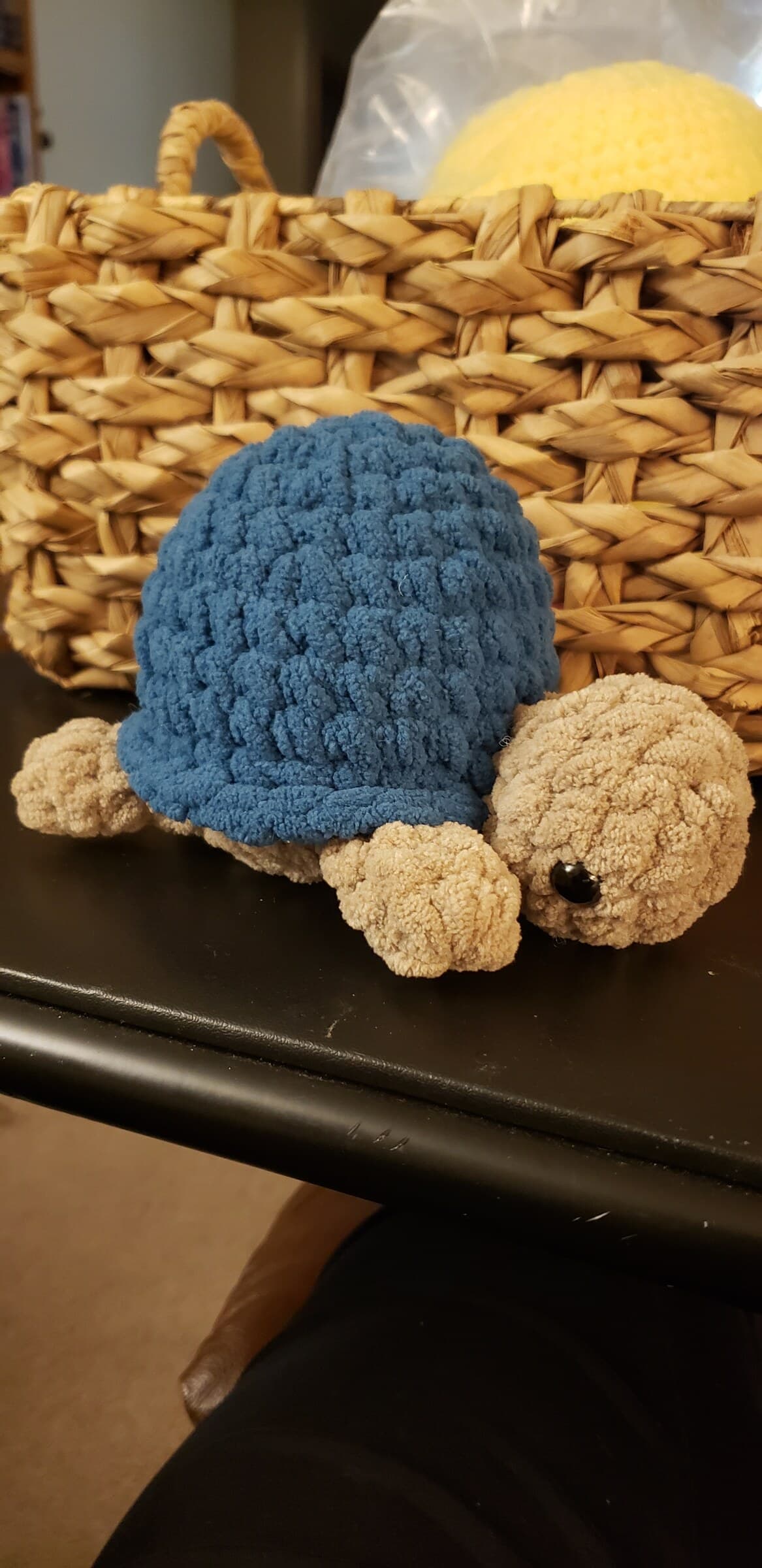 A handmade blue and tan crocheted turtle plushie beside a woven basket.