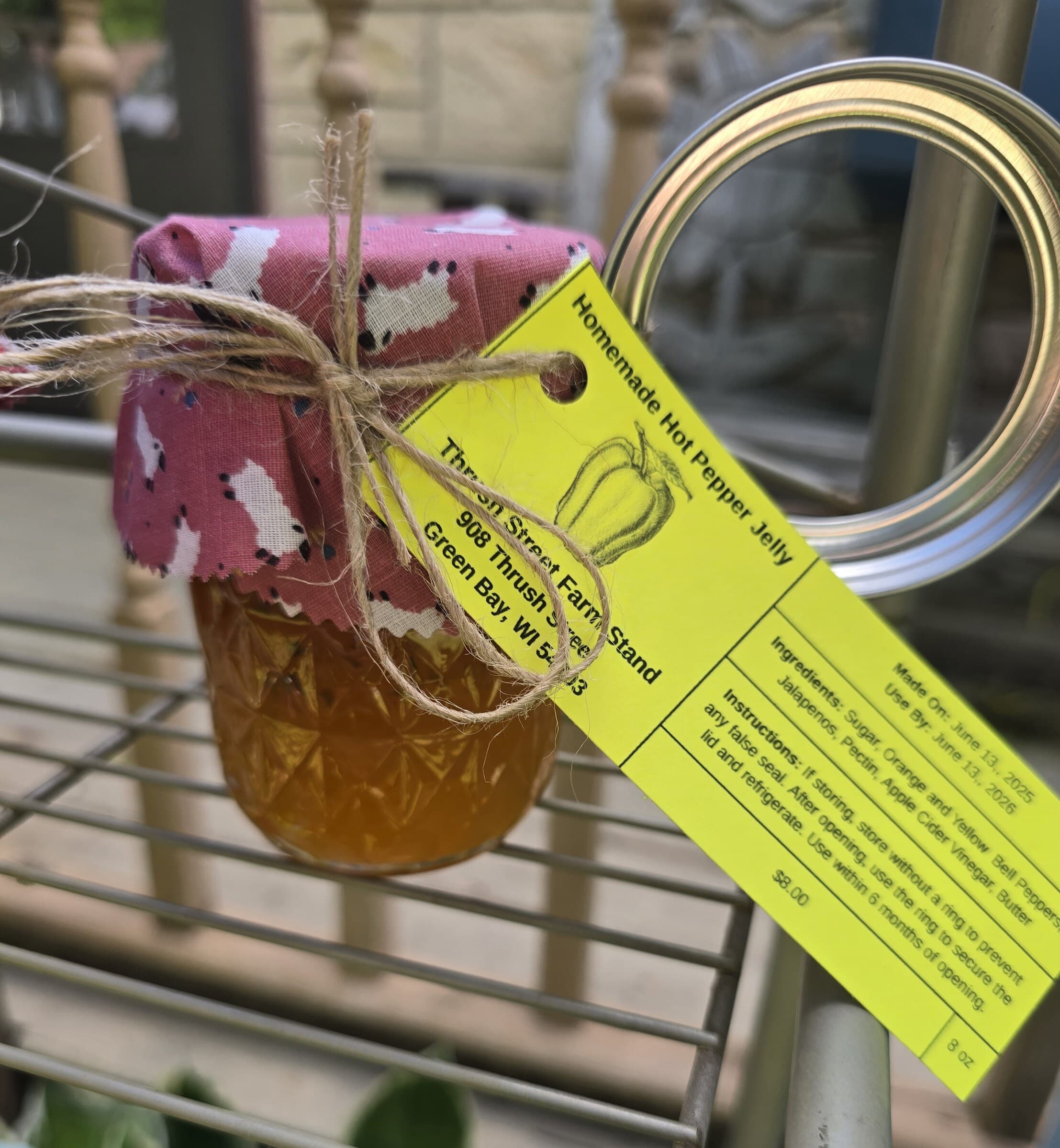 A jar of homemade hot pepper jelly with a pink fabric top and ingredient tag.
