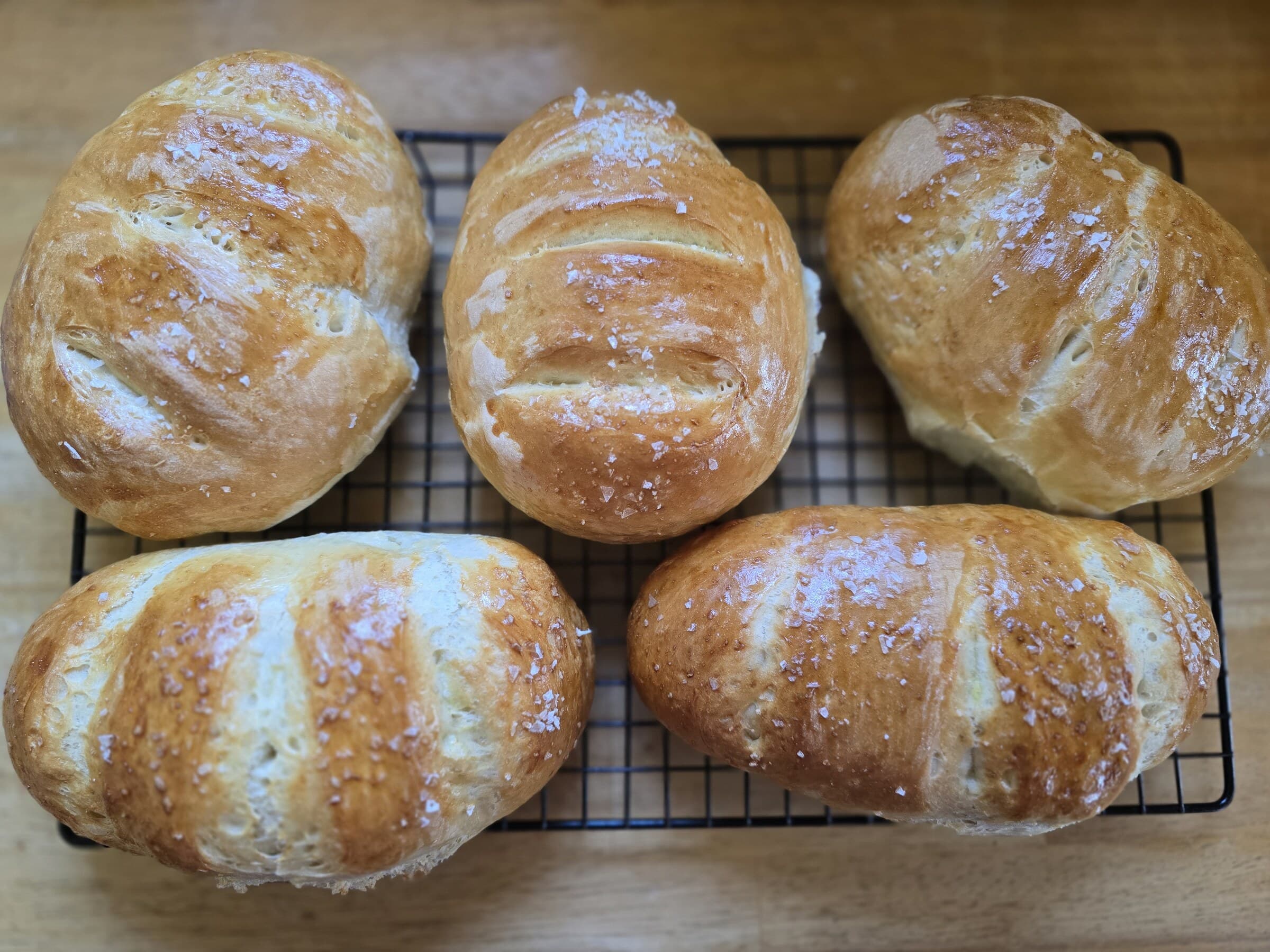 Five golden French bread loaves cooling together on a wire rack.
