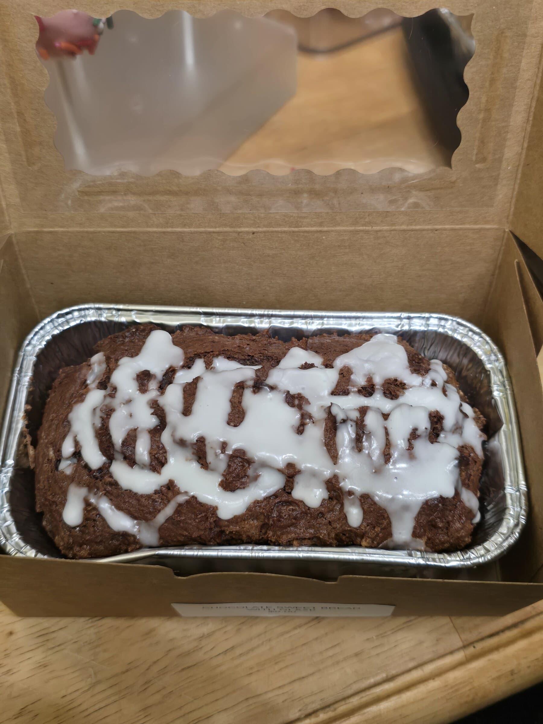 A chocolate sweet bread loaf finished with white icing in a bakery box.