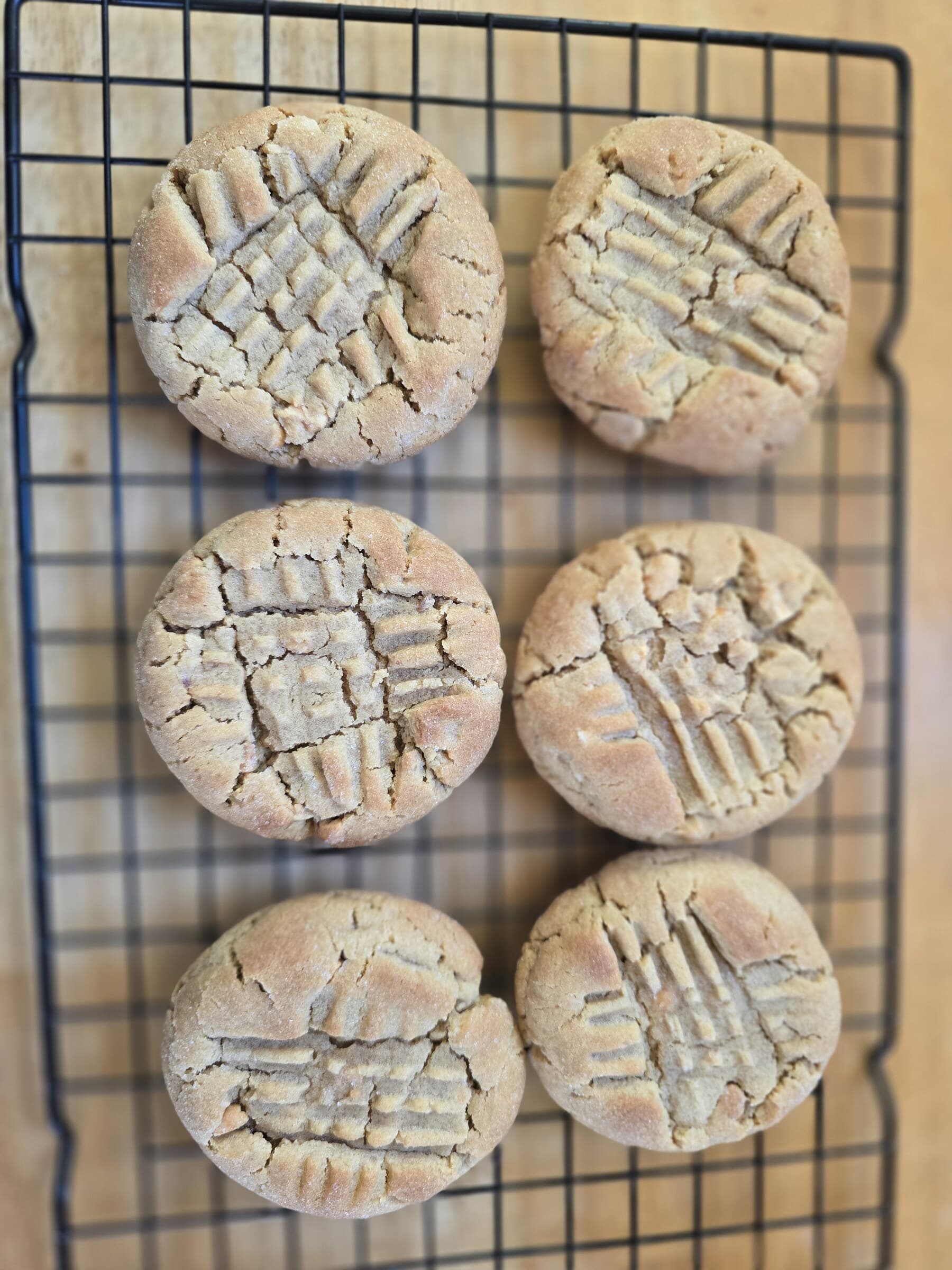 Six peanut butter cookies with fork-marked tops cooling on a wire rack.