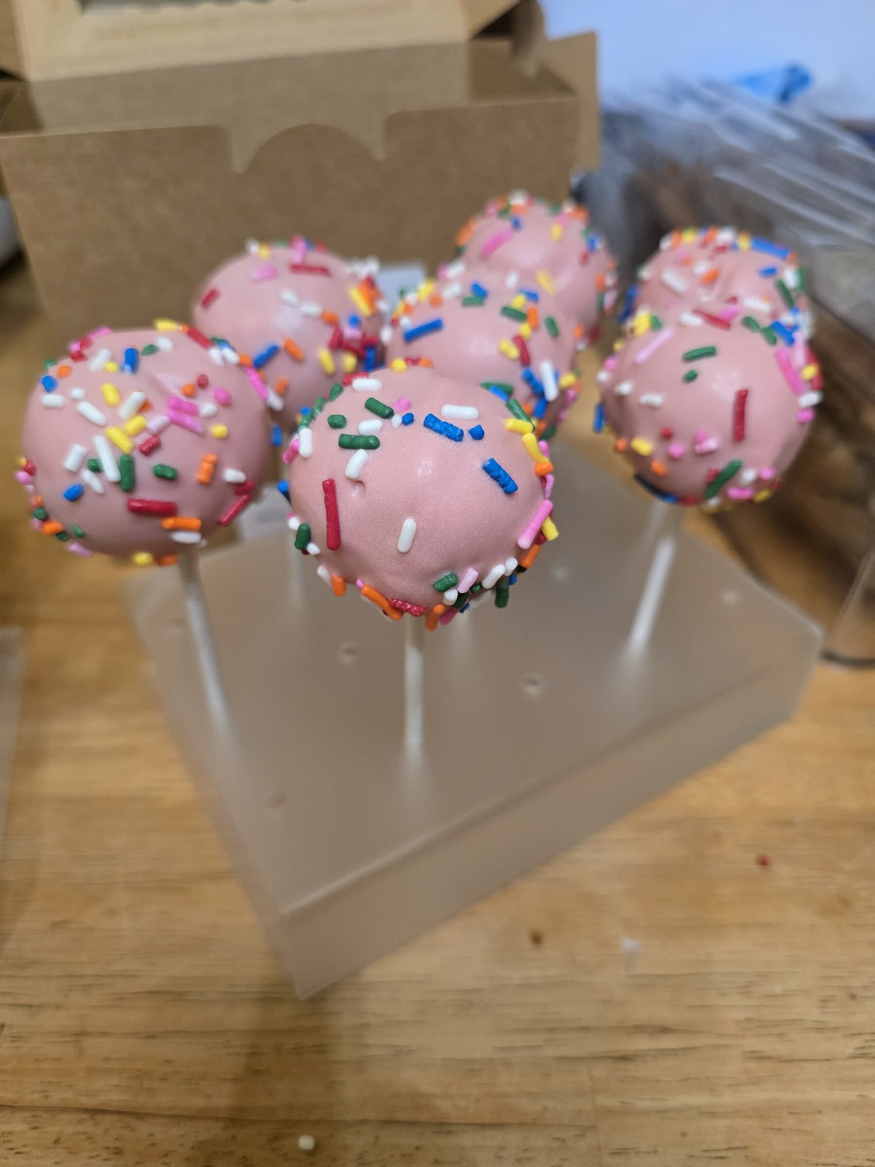 Pink strawberry cake pops decorated with rainbow sprinkles.