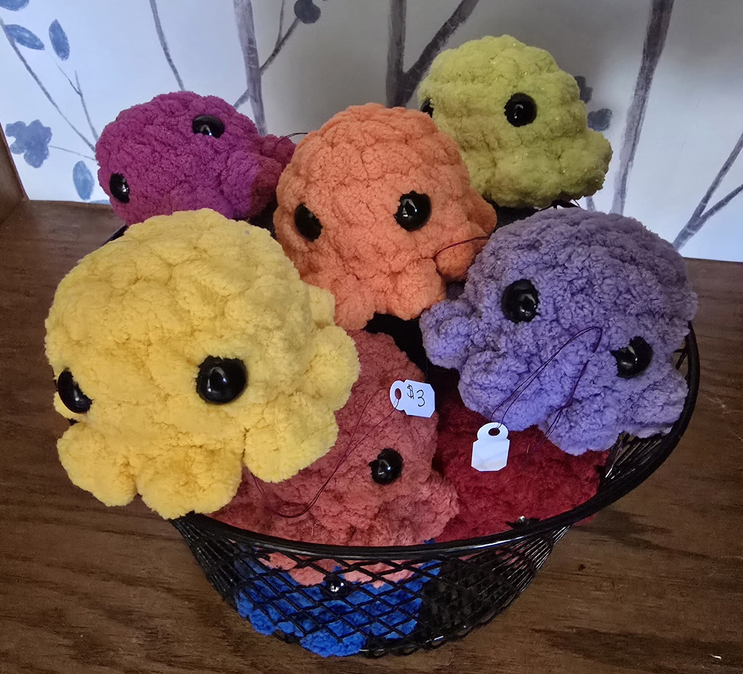 A wire basket full of mini crocheted octopus plushies in bright rainbow colors.