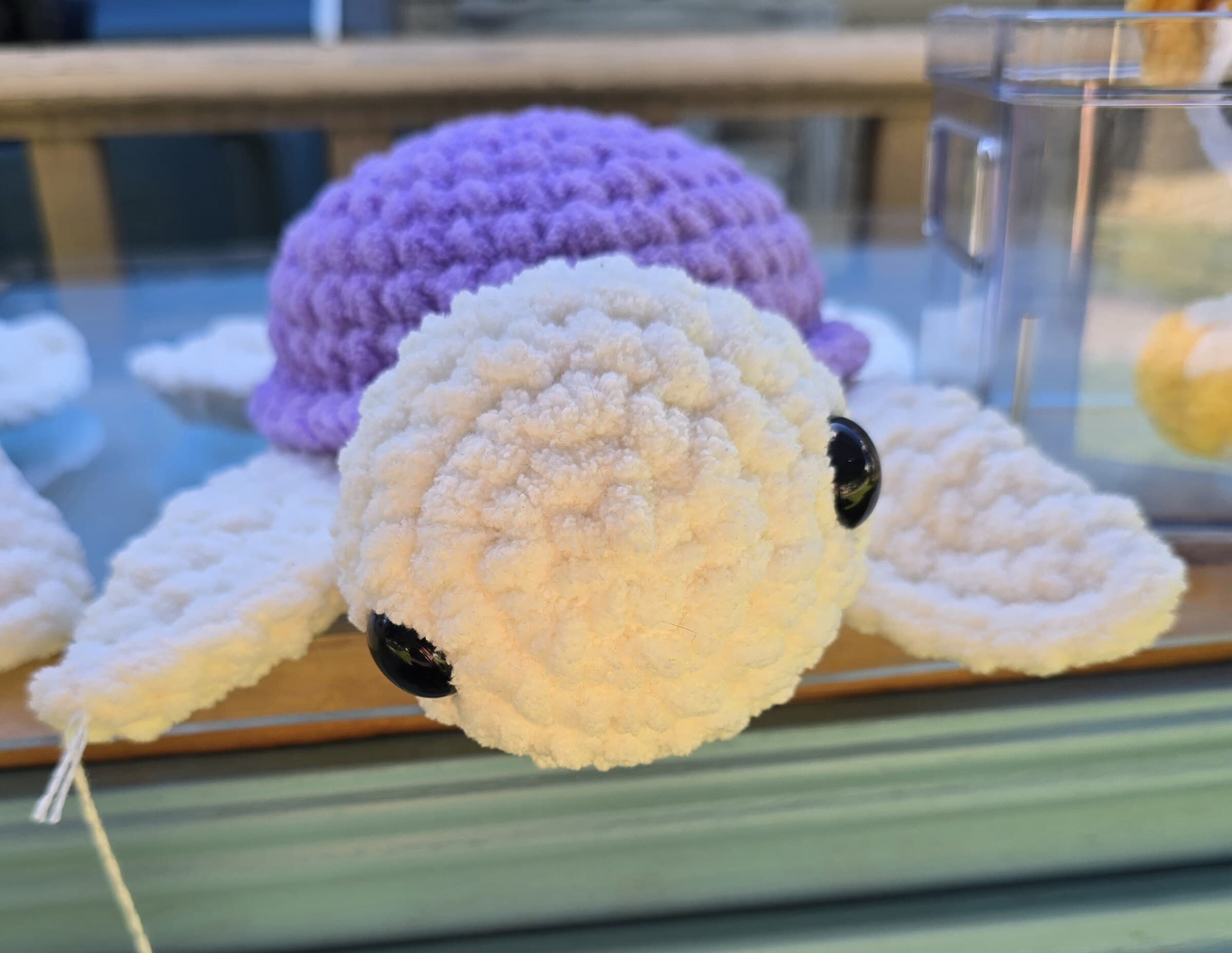 A purple and white crocheted turtle plushie resting on the farm stand counter.